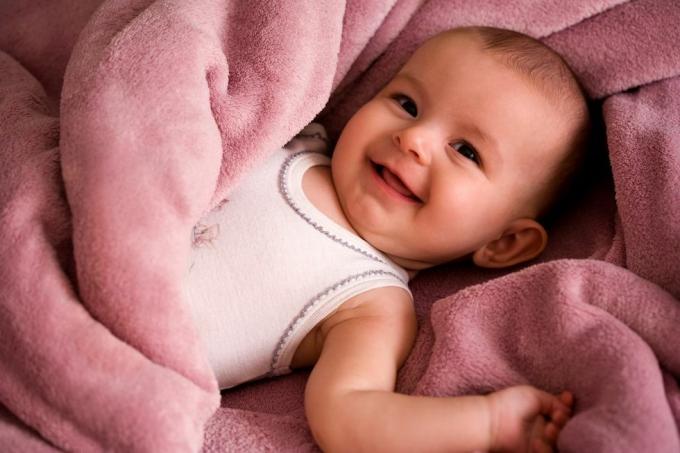 portret van baby in een wit overhemd in tankstijl glimlachend en gewikkeld in een zachtroze deken