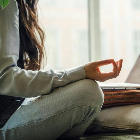 een aziatische vrouw van middelbare leeftijd in spijkerbroek zittend op het bed in een yogahouding voor een laptop op afstand werken thuis online winkelen in quarantaineperiode