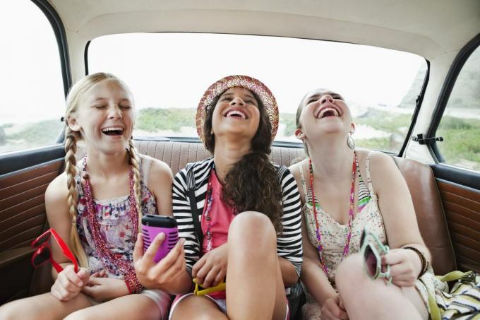 drie lachende meisjes op de achterbank van een auto