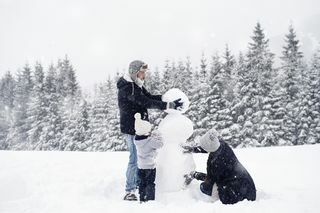 gezin van drie die een sneeuwpop bouwen in de sneeuw