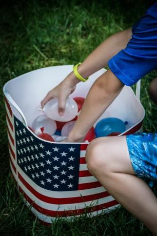 kind plukken van kleine rode, witte en blauwe waterballonnen uit bad met Amerikaanse vlag erop