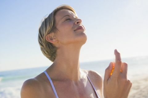 Vrouwen bespuitend parfum op haar hals op het strand