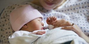 pasgeboren meisje met roze muts, ingebakerd in een deken met moeder vanaf de kin gezien in een ziekenhuisjas die haar vasthoudt