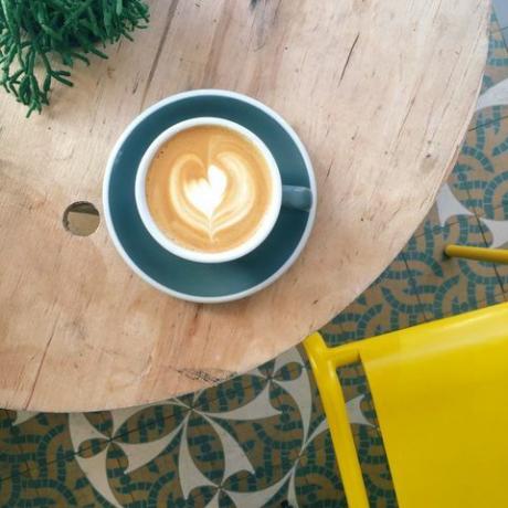 Kopje koffie met hart schuim in groenblauw mok op houten tafel