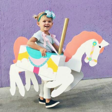 klein meisje met een doos in de vorm en geschilderd om eruit te zien als een carrouselpaard om haar heen