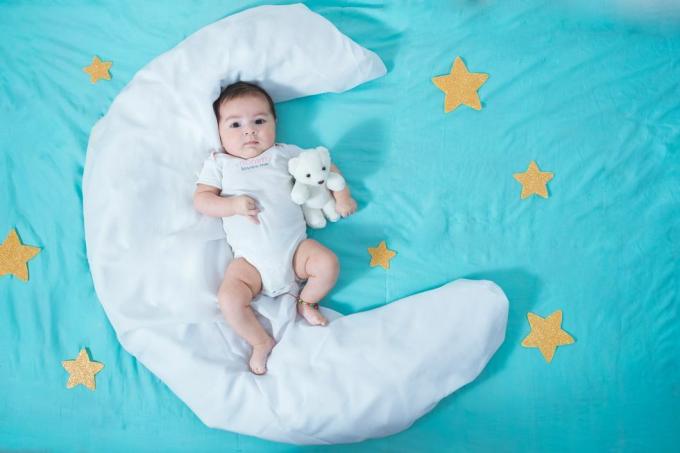 mooi latijns babymeisje, twee maanden oud, liggend op een wit laken in de vorm van een maan met gele sterren aan elke kant en een blauw laken eronder