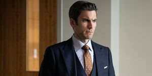 Wes Bentley in een donkergrijs driedelig pak met een bruine bedrukte stropdas en een wit met blauw gestreept overhemd staat in een kantoor met zijn handen in zijn zakken