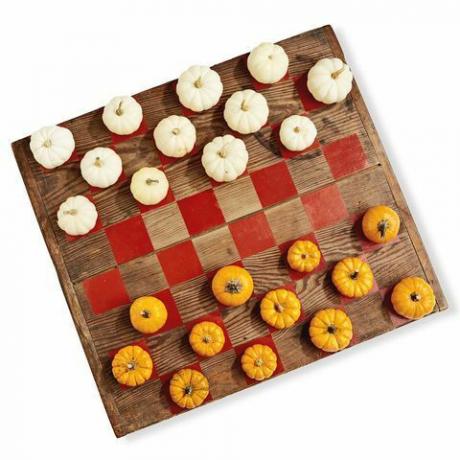 een houten bord geschilderd als een damspel met minipompoenen in wit en oranje als speelstukken