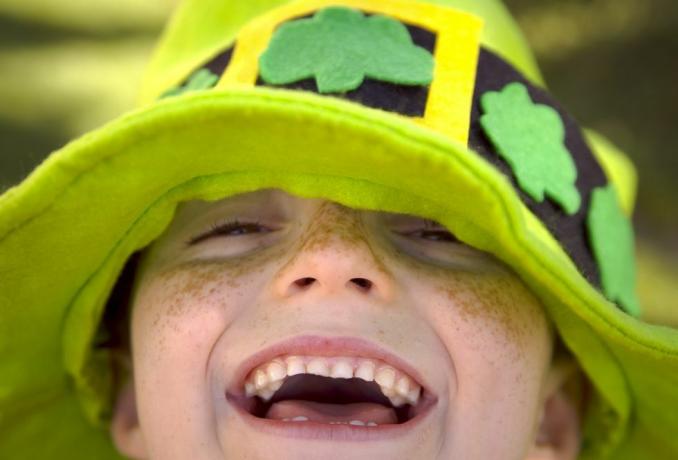 close-up van een lachend kind met sproeten op st patrick's day in een groen randje met klavers dat een schattig onderschrift nodig heeft