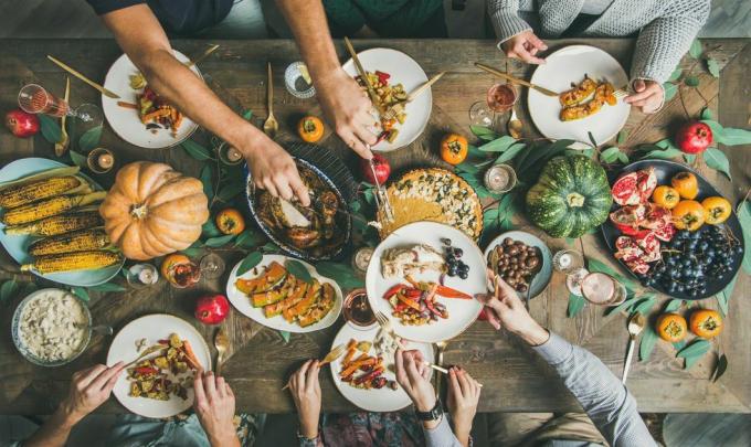 bovenaanzicht van Thanksgiving-dagtafel met kalkoen, pompoentaart, geroosterde seizoensgroenten en fruit en mensen die borden vullen en eten