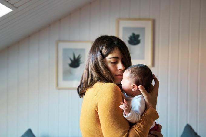 Zijaanzicht van nieuwe moeder die haar pasgeboren baby troost terwijl ze huilt en de baby gewend raakt aan geluiden en licht in haar eerste dagen van leven buiten de baarmoeder