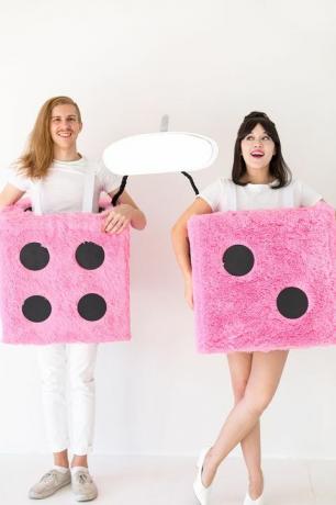 man en vrouw verkleed als roze pluizige dobbelstenen bevestigd aan een grote zelfgemaakte achteruitkijkspiegel