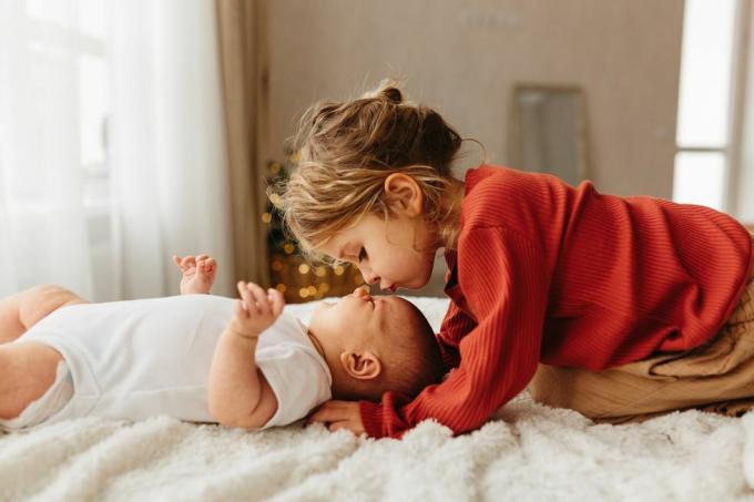 schattig kind zoenen zusje liggend op wit beddengoed