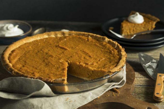 zelfgemaakte zoete aardappeltaart met één stuk eruit gesneden op tafel naast stuk taart met slagroom en kom slagroom op de achtergrond