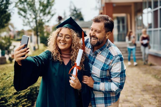 gelukkige universitair afgestudeerde en haar vader hebben plezier terwijl ze een selfie maken met een smartphone