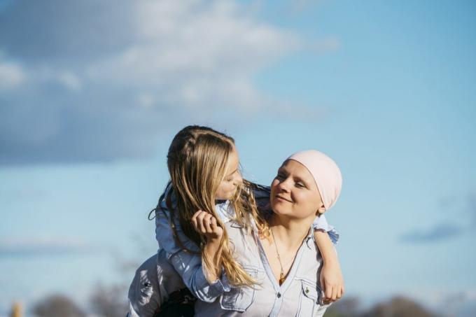 vrouw gezien van kin tot buik die haar handen uitstrekt om een ​​hartvorm te maken om een ​​roze lint op haar witte trui te omlijsten