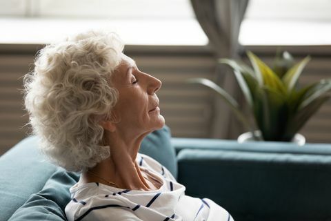 zijaanzicht close-up gezicht van volwassen kalme vrouw uit de jaren 60 gesloten ogen genieten van frisse lucht thuis tijd doorbrengen leunend op de bank, rustend mentale en fysieke kracht opdoen mindfulness meditatie voor senioren concept