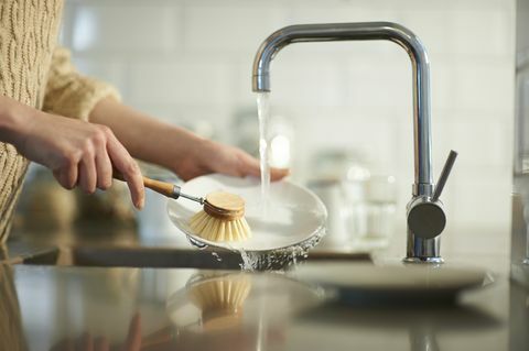een vrouw gebruikt een plasticvrije borstel om de vaat in een gootsteen schoon te maken, van dichtbij