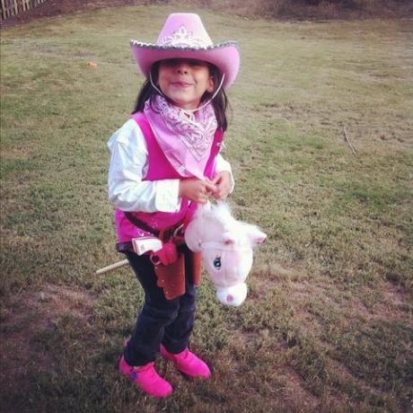 klein meisje helemaal in het roze gekleed als een cowgirl met een stokpaardje