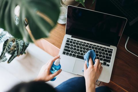 bijgesneden opname van een jonge vrouw die het oppervlak van de laptop schoonmaakt met reinigingsspray en antistatische doek thuis