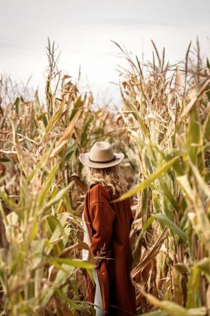stijlvolle vrouw met rode jas en hoed staat in maïsveld