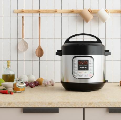 multicooker op aanrecht met uien, knoflook, bakolie en snijplank