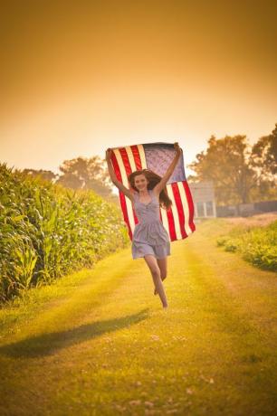 tiener boerderij meisje loopt door veld zwaaien ons vlag