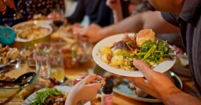 man serveert zichzelf aan een eettafel, er liggen groenten en een koekje op zijn bord