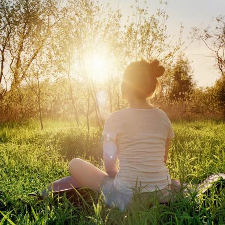 jonge vrouw zittend in yoga-positie genieten van zonsondergang in de natuur