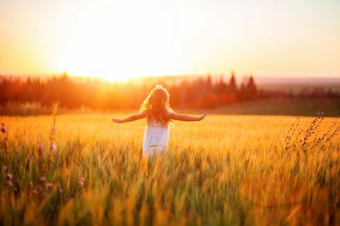 klein meisje in witte jurk in veld bij zonsondergang