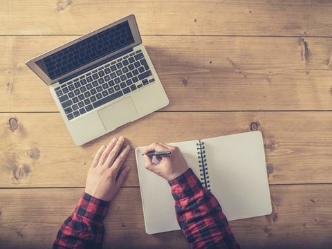 overhead shot van een man die in een notitieblok schrijft met een laptop naast hem