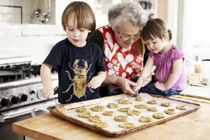 oma en twee jonge kleinkinderen die de kleindochter bakken, leggen met grootmoeders hulp deeg op een bakplaat