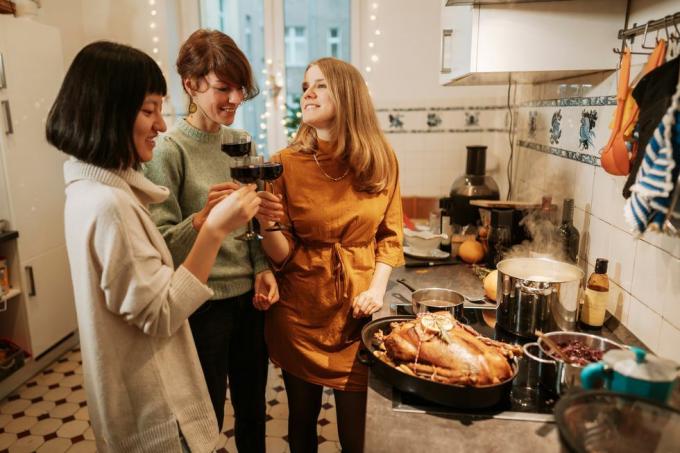 drie vrouwen die rode wijn drinken terwijl ze thuis een kalkoenmaaltijd bereiden met een kalkoen en drie potten op het fornuis