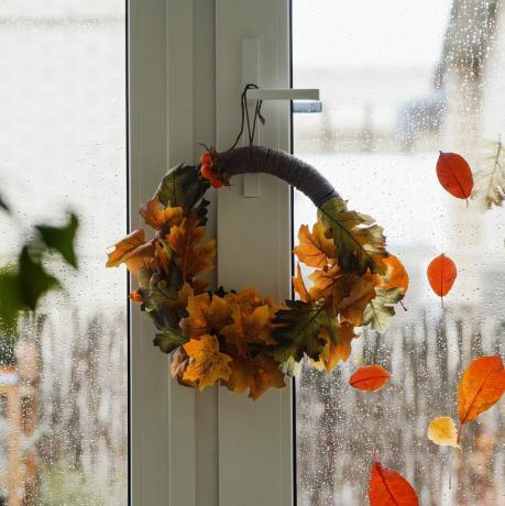 diy herfstkrans van kleurrijke rode, bruine en gele bladeren op het raam op regenachtige herfstdag