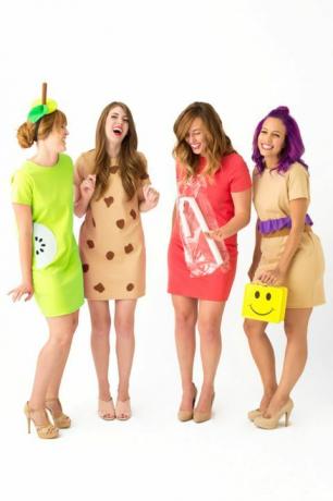 vier lachende vrouwen in korte jurken verkleed als 'lunchdames', een met een gele lunchtrommel met smileygezicht